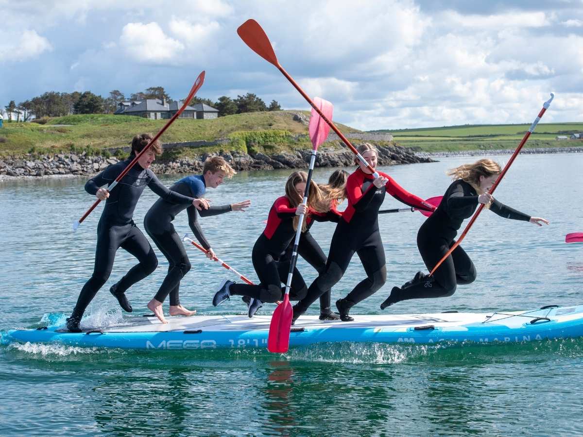 Youth Club Giant SUP Fenit Kerry Youth group balancing and paddling together on a giant SUP during a water activity session in Fenit, Co. Kerry